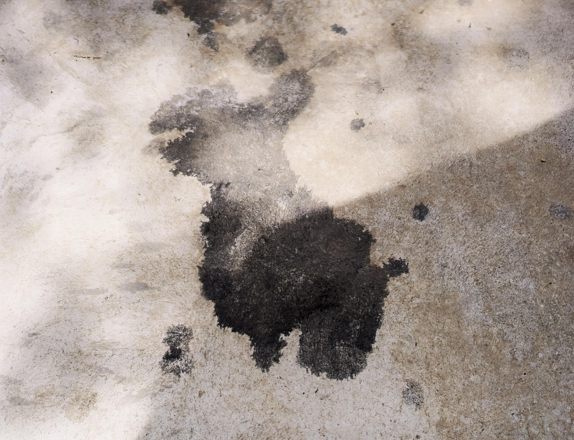 A weathered concrete wall with dark soot stains and uneven beige tones at the surface edge.