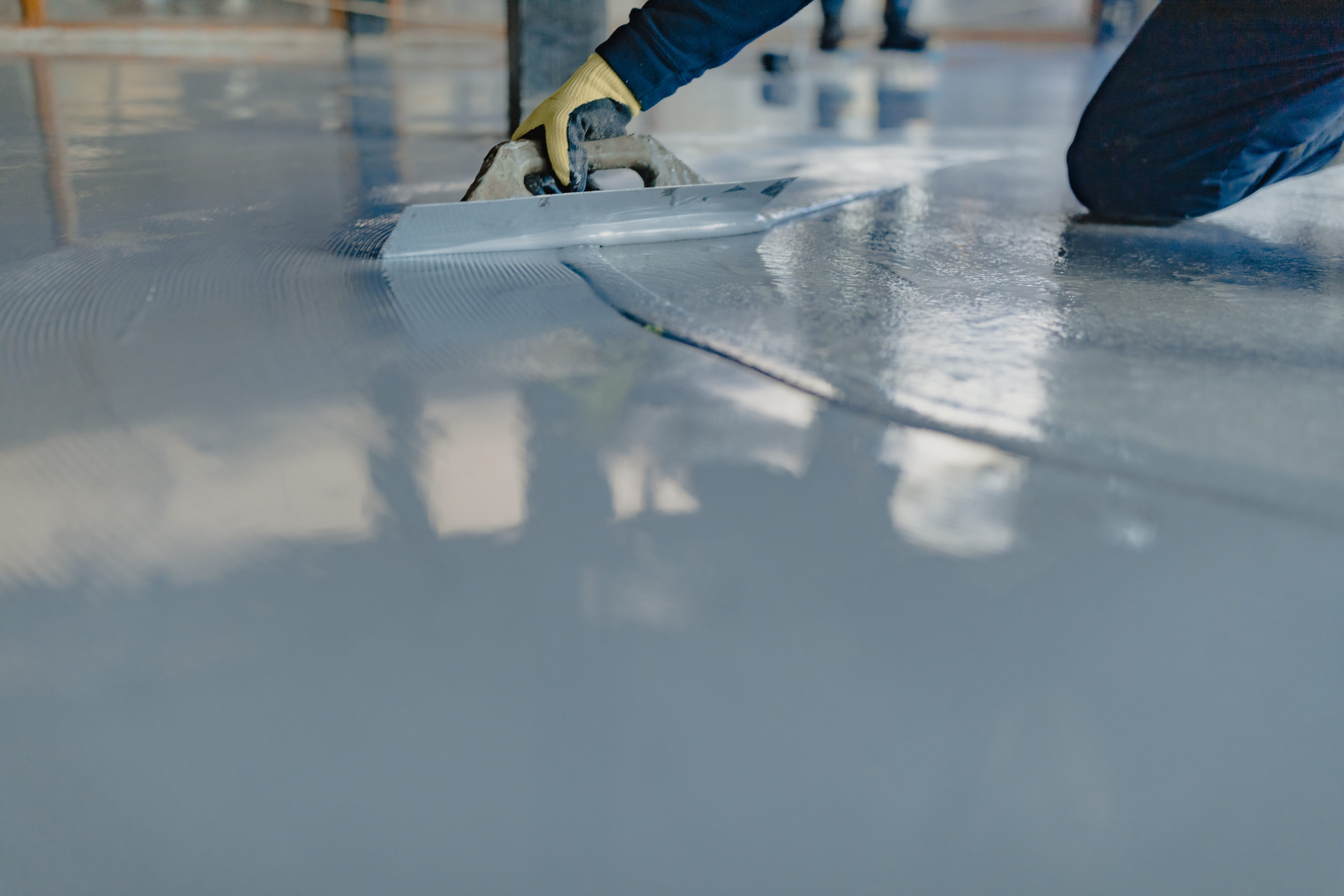 A worker applies a smooth layer of gray epoxy resin to a floor using a trowel, creating the best garage floor coating for lasting durability and sleek appearance.